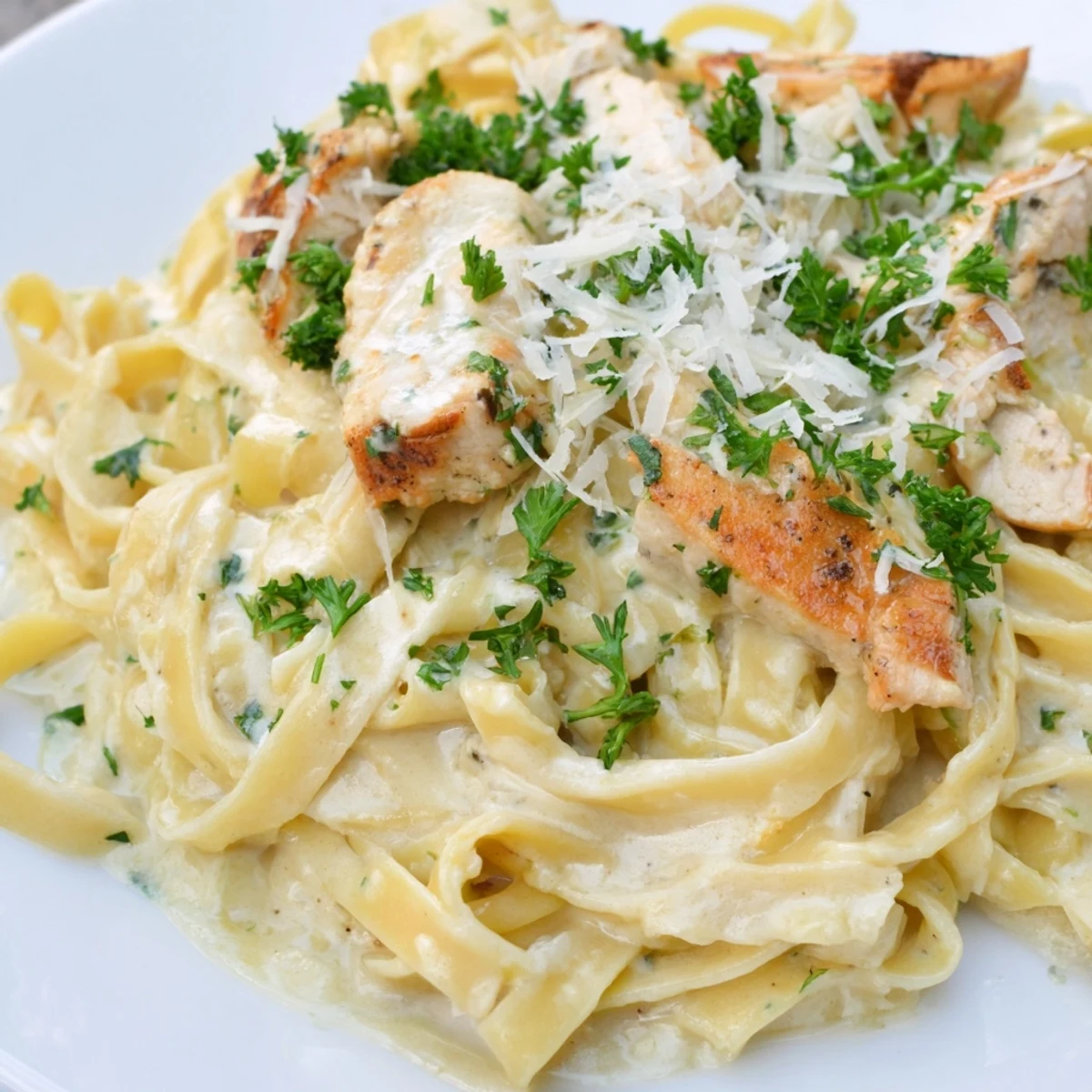 Creamy Chicken Alfredo pasta is served with tender golden chicken strips draped in a rich Parmesan cream sauce over fettuccine noodles.