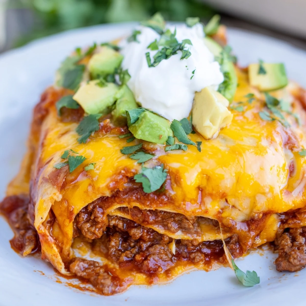 Sliced serving of Beef Enchilada Casserole topped with creamy sour cream and diced avocado.