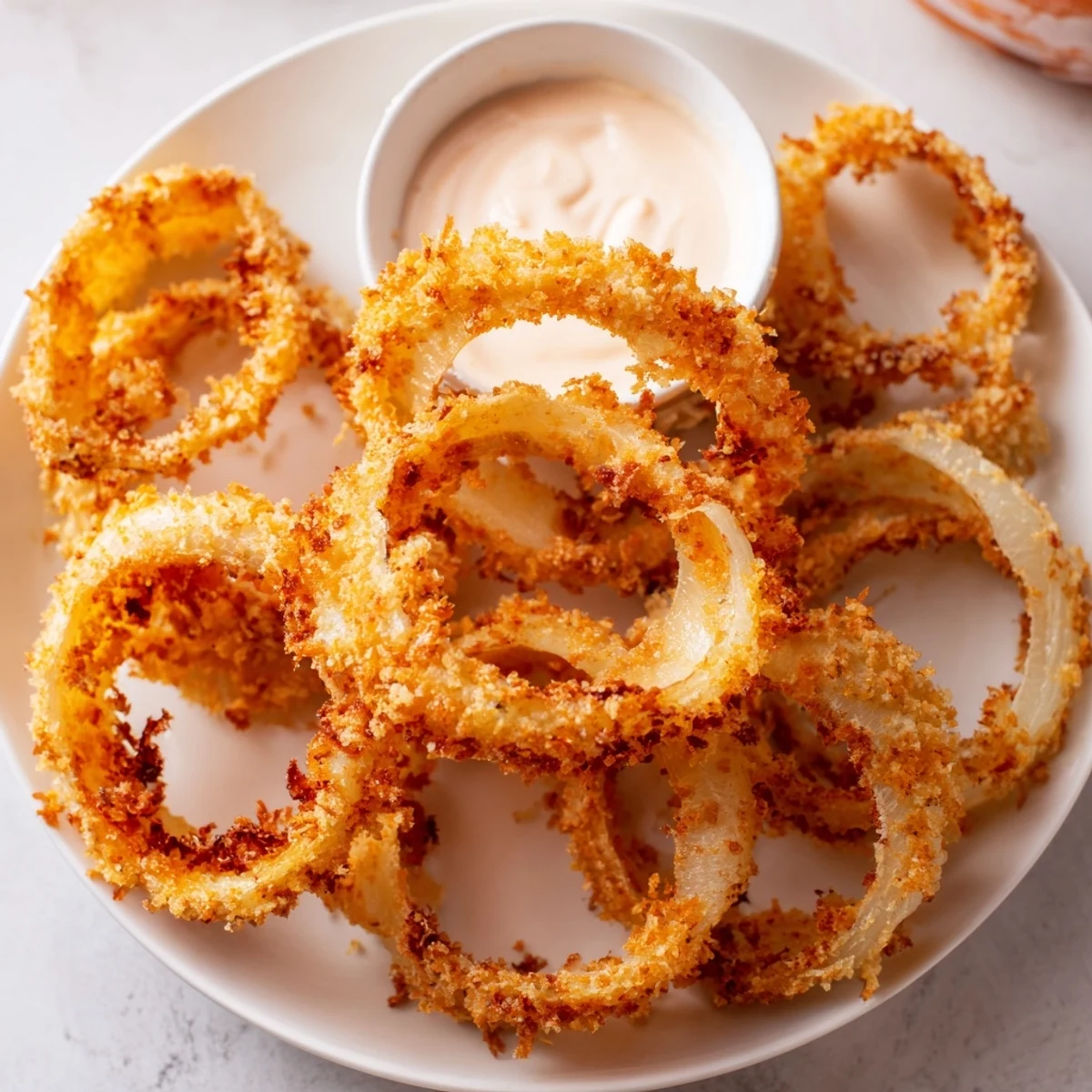Golden, crispy Crispy Onion Rings with Spicy Mayo Dipping Sauce stacked on a white plate, ready for dipping.  