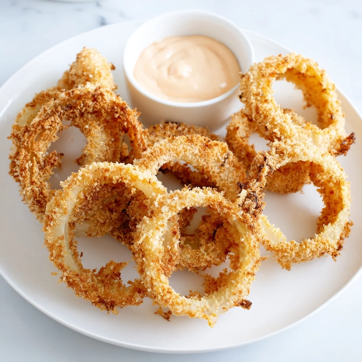 A platter of golden brown Crispy Onion Rings with Spicy Mayo Dipping Sauce garnished with fresh parsley.
