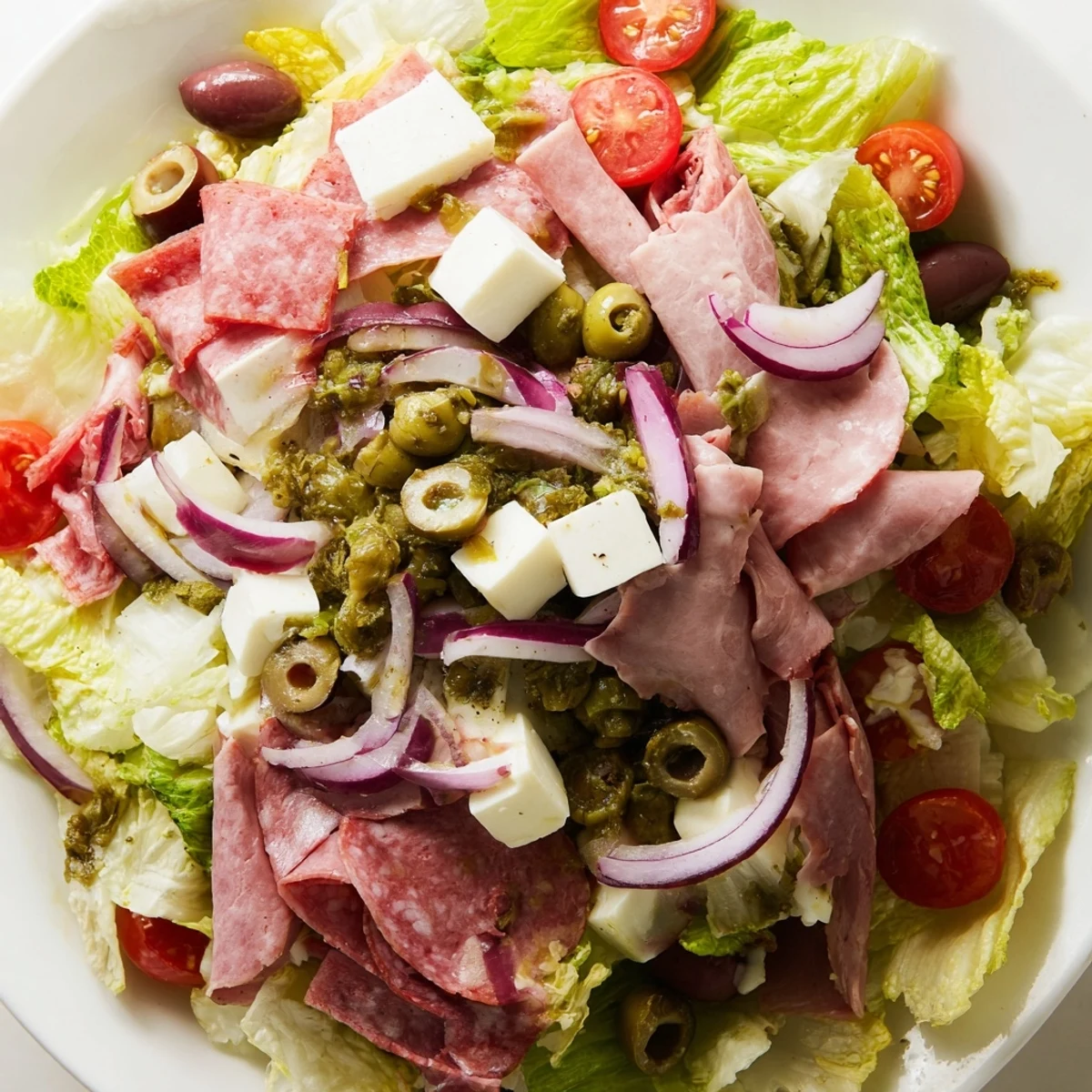 Colorful bowl of New Orleans Muffuletta Salad with cubed mozzarella, tomatoes, and zesty pepperoncini garnished with fresh basil.