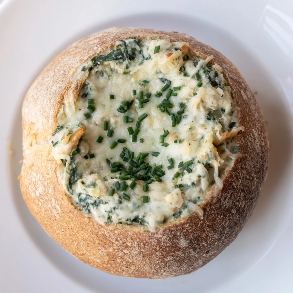 Freshly baked Spinach Dip in a sourdough bread bowl is ready to serve, with torn bread pieces and vegetable dippers alongside.