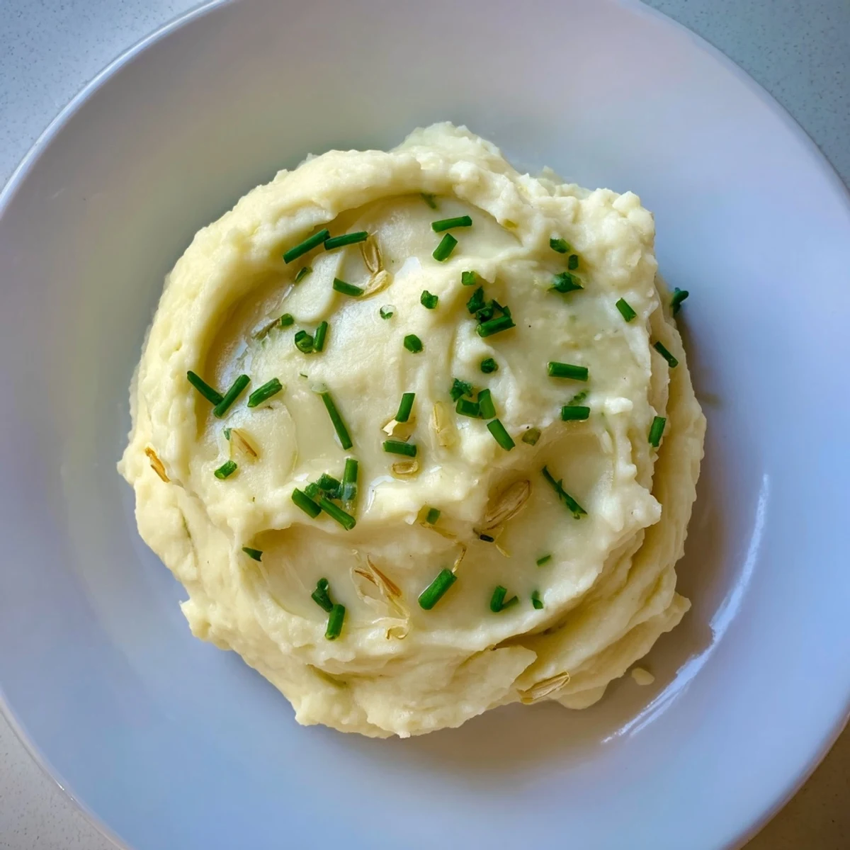Creamy roasted garlic mashed cauliflower served warm in a rustic white bowl topped with fresh chives.