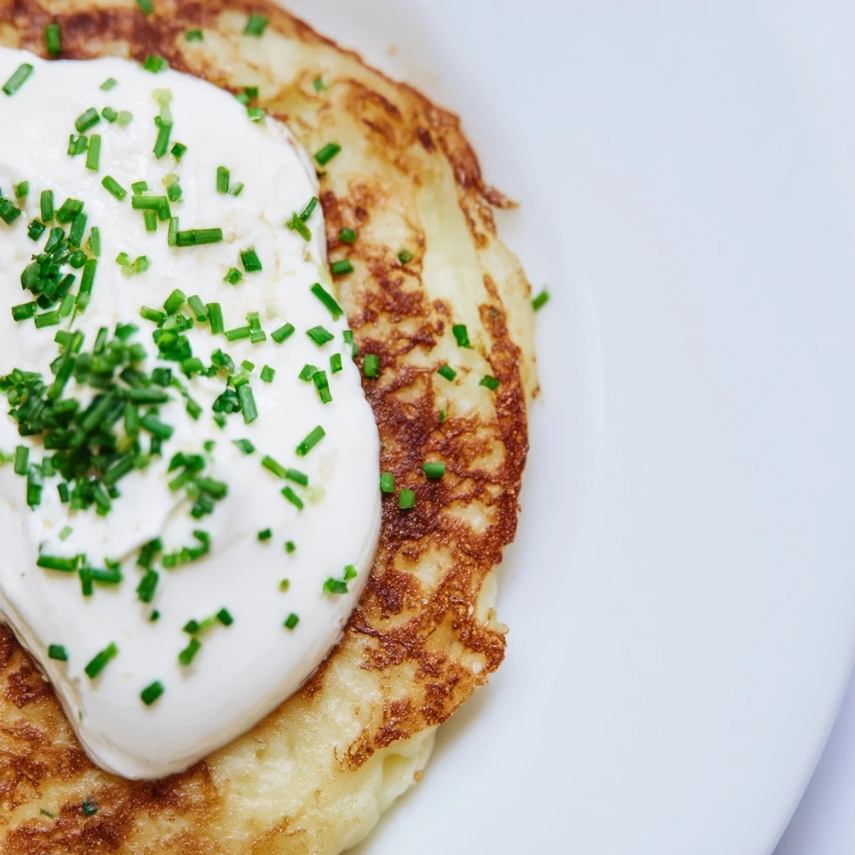 Warm Irish Boxty with Sour Cream and Chives served on a white plate, ready to be enjoyed as a snack.