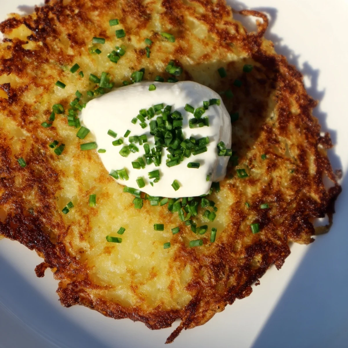 Golden-brown Irish Boxty with Sour Cream pancakes are stacked on a plate, topped with a dollop of cool sour cream and fresh chives.