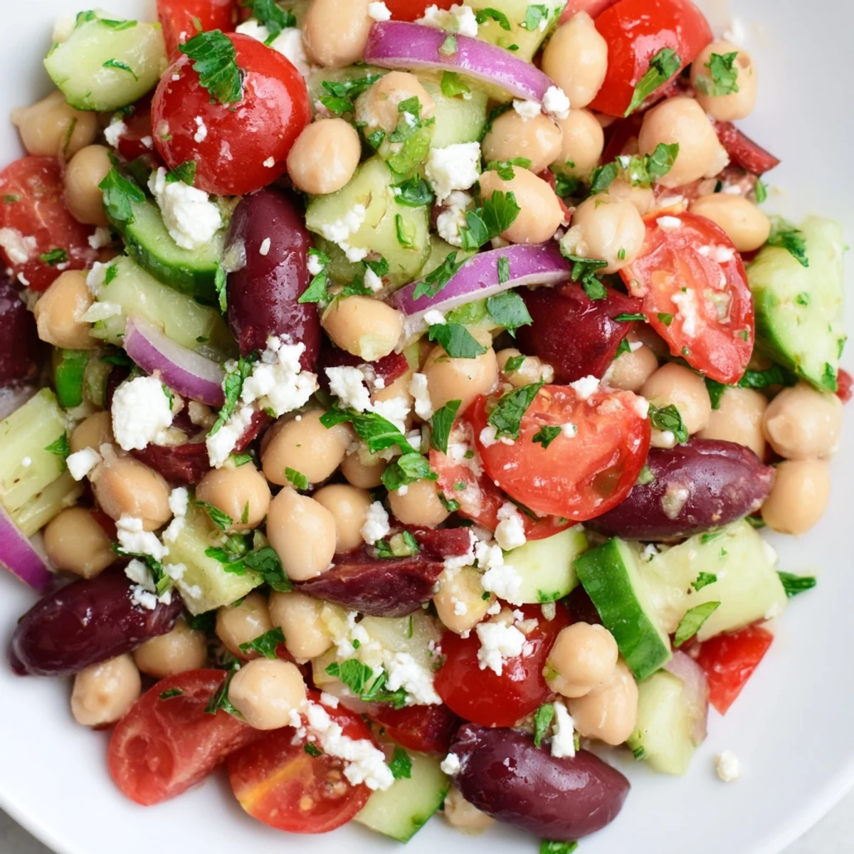 Close-up of a vibrant Mediterranean Dense Bean Salad in a white ceramic bowl, showcasing chickpeas, tomatoes, and crumbled feta.