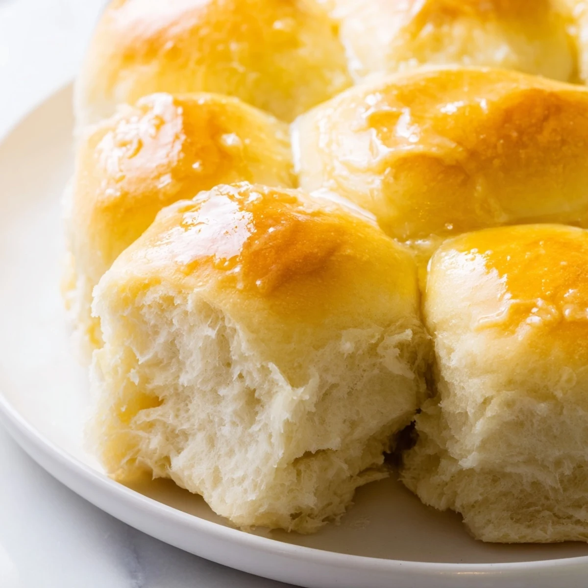 Warmly baked golden Best Vegan Dinner Rolls brushed with melted vegan butter on a white ceramic plate.