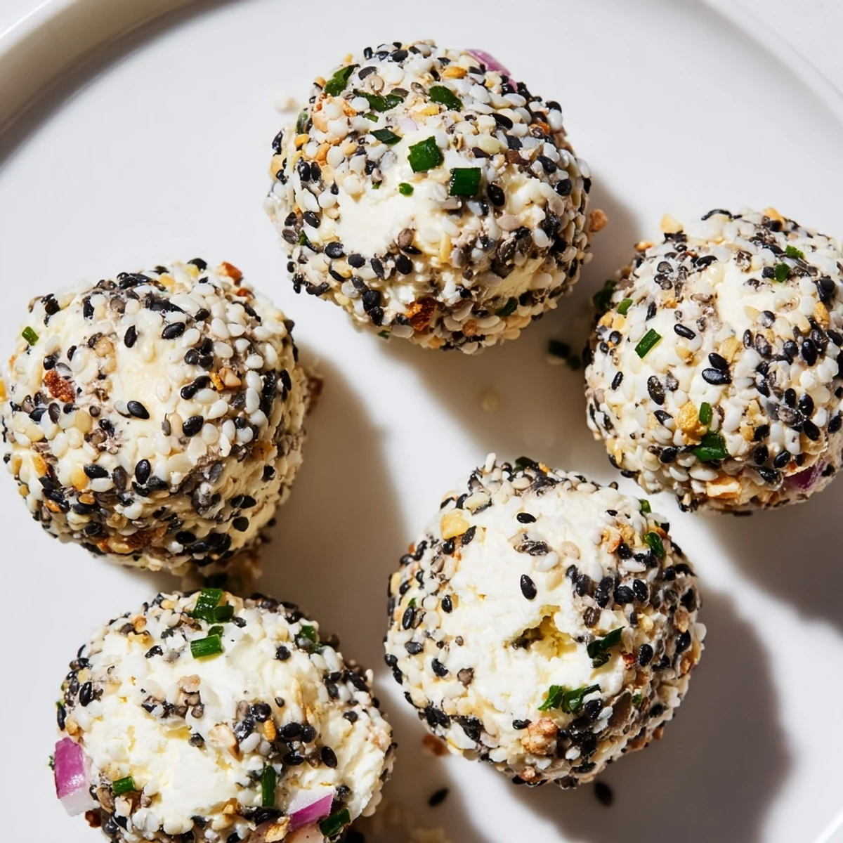 Creamy Everything Bagel Cottage Cheese Bites coated in sesame and poppy seeds on a white platter with fresh chives.