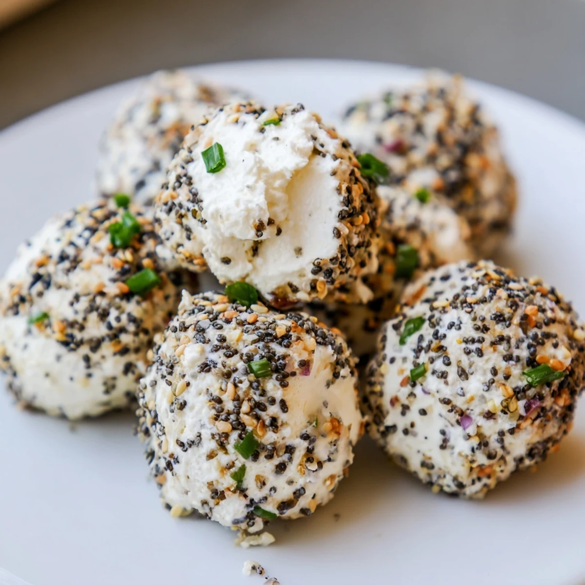 Bite-sized Everything Bagel Cottage Cheese Bites arranged on a serving plate, garnished with red onion and chives for appetizers.