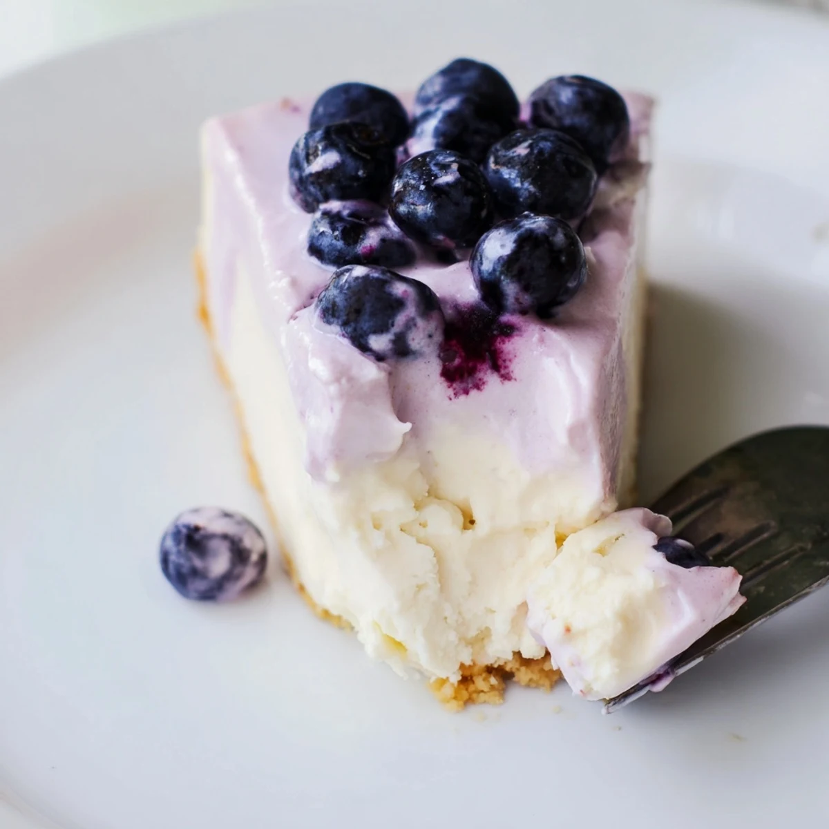 Rich Blueberry Mousse Cheesecake served with a dessert fork, featuring a creamy texture and vibrant blueberry sauce.