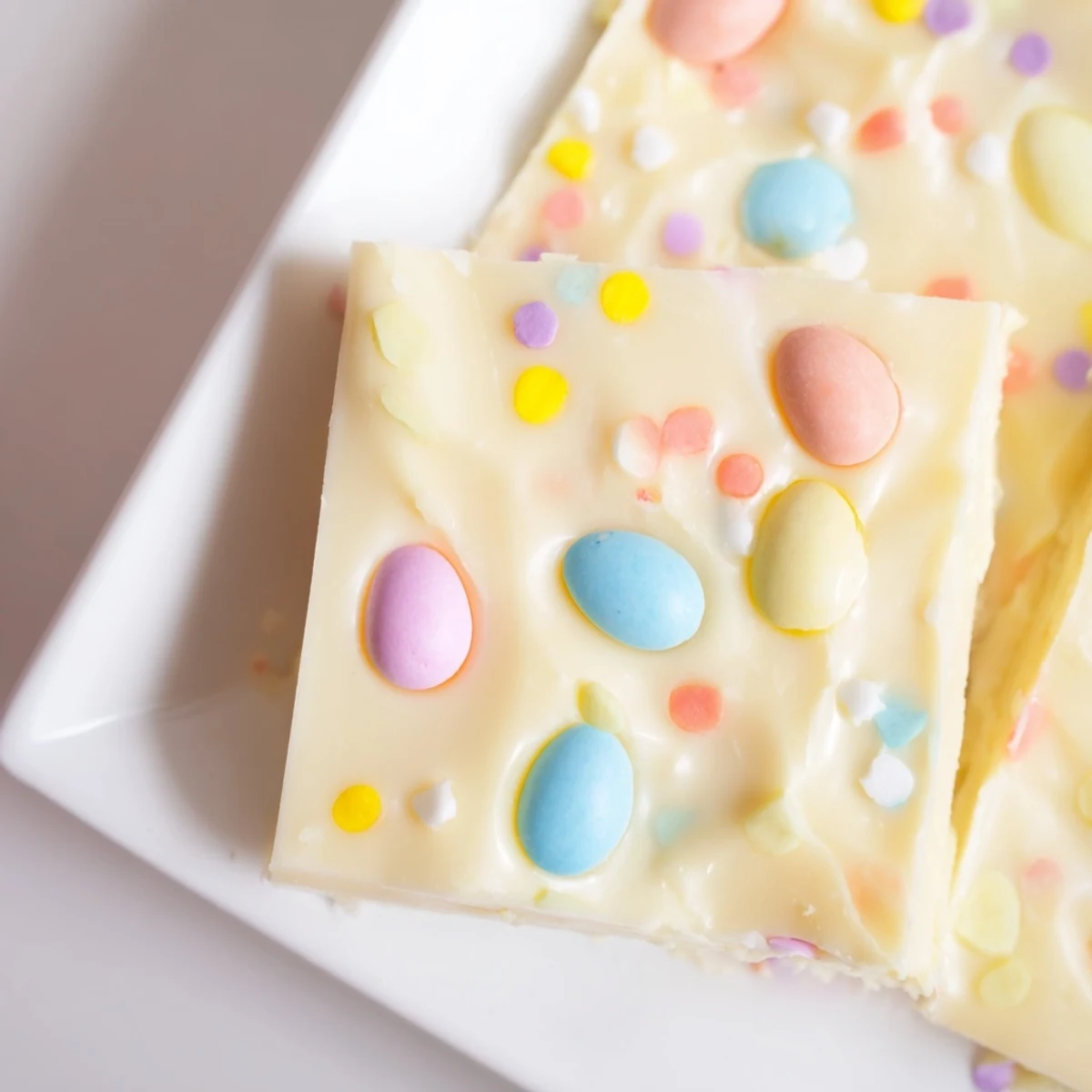 A close-up of homemade Easter Fudge squares studded with pastel candy eggs and sprinkles on a marble countertop.