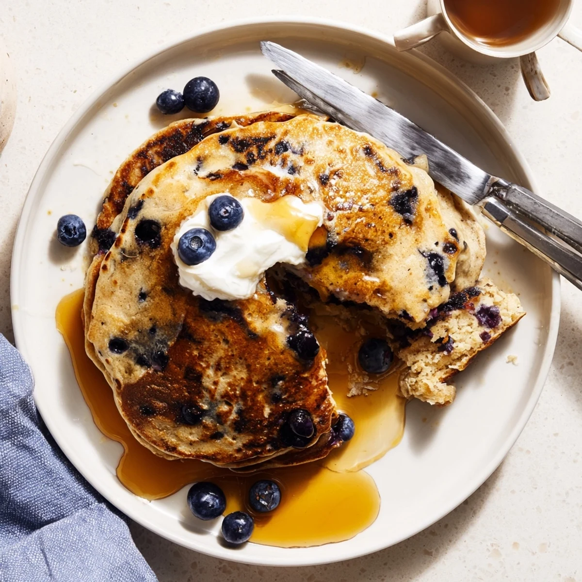 Overhead view of Fluffy Greek Yogurt Blueberry Pancakes served with butter and syrup on a white ceramic plate.