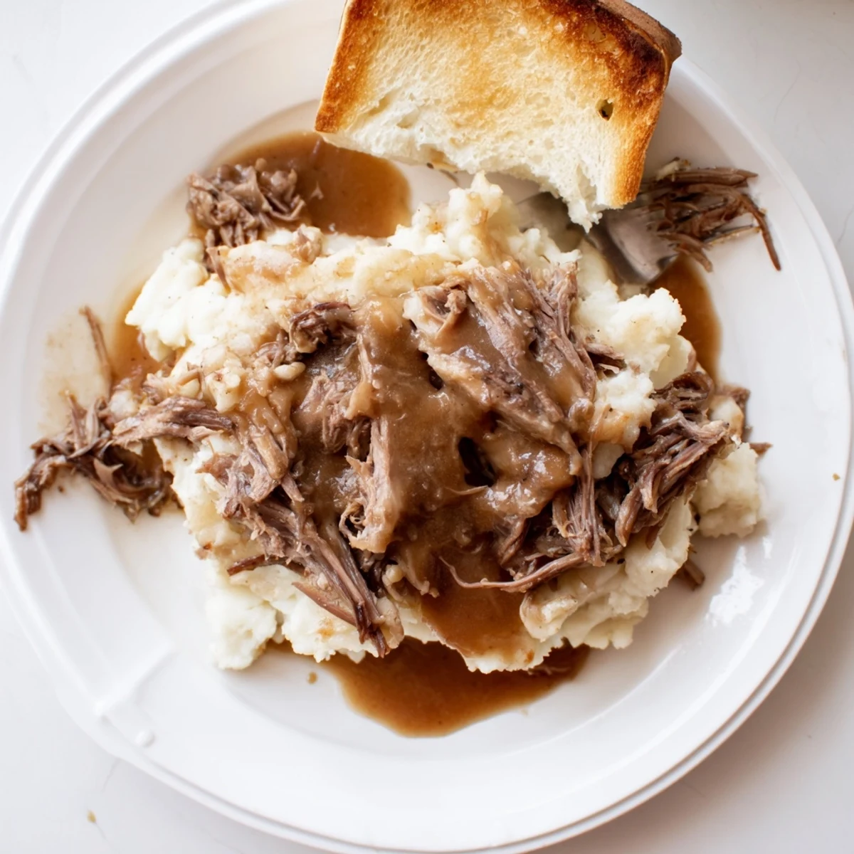 Shredded Slow Cooker Beef Manhattan topped with creamy mashed potatoes and rich brown gravy over thick bread.