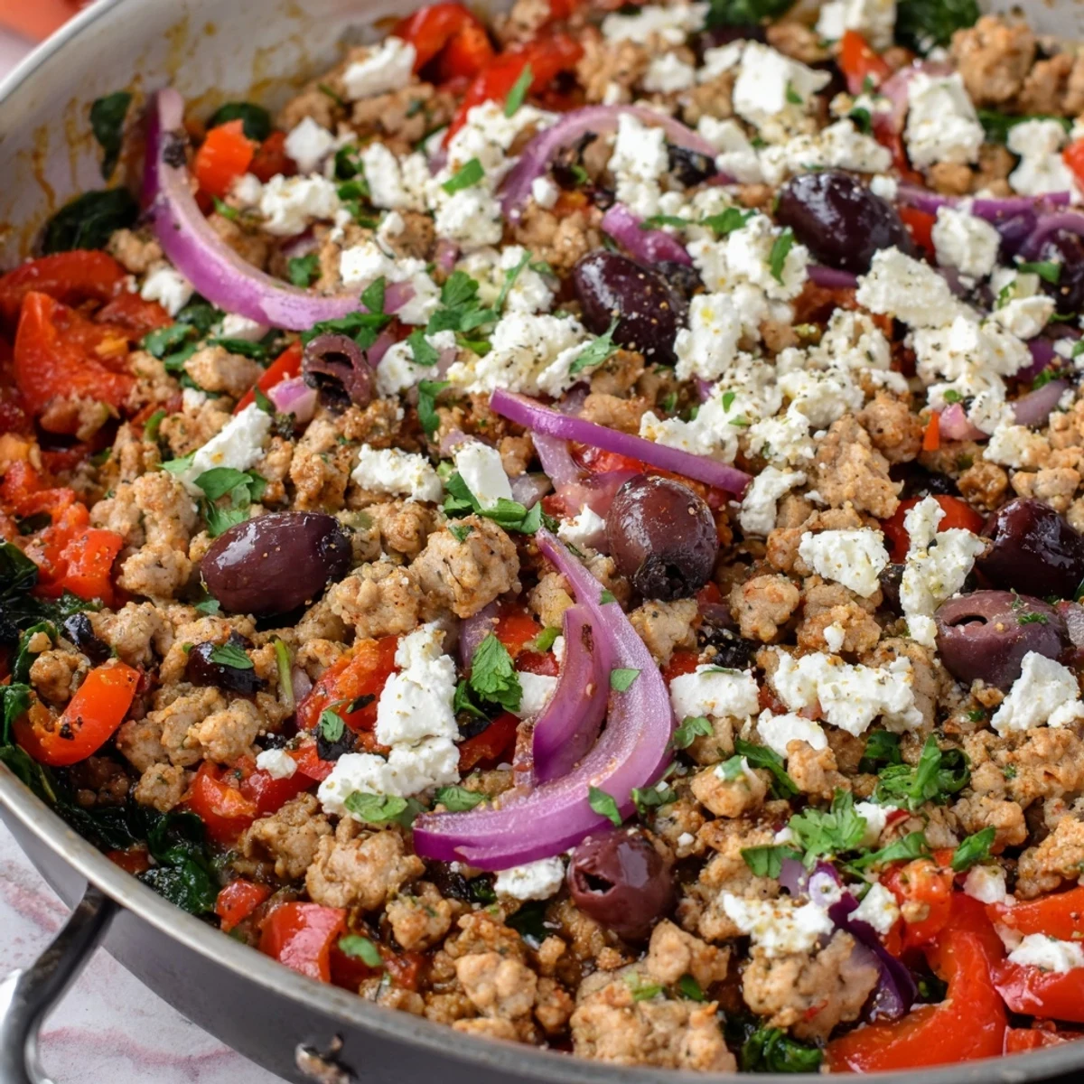 A close-up reveals juicy ground chicken, Kalamata olives, and creamy feta in a vibrant skillet dinner.  