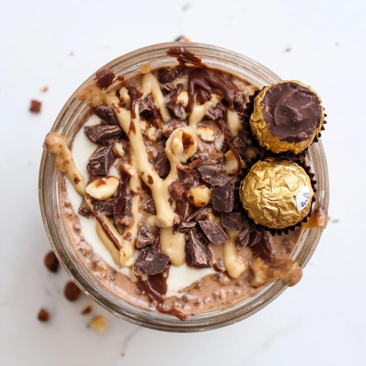 Ferrero Rocher Protein Overnight Oats layered in a glass jar topped with chopped hazelnuts and dark chocolate.
