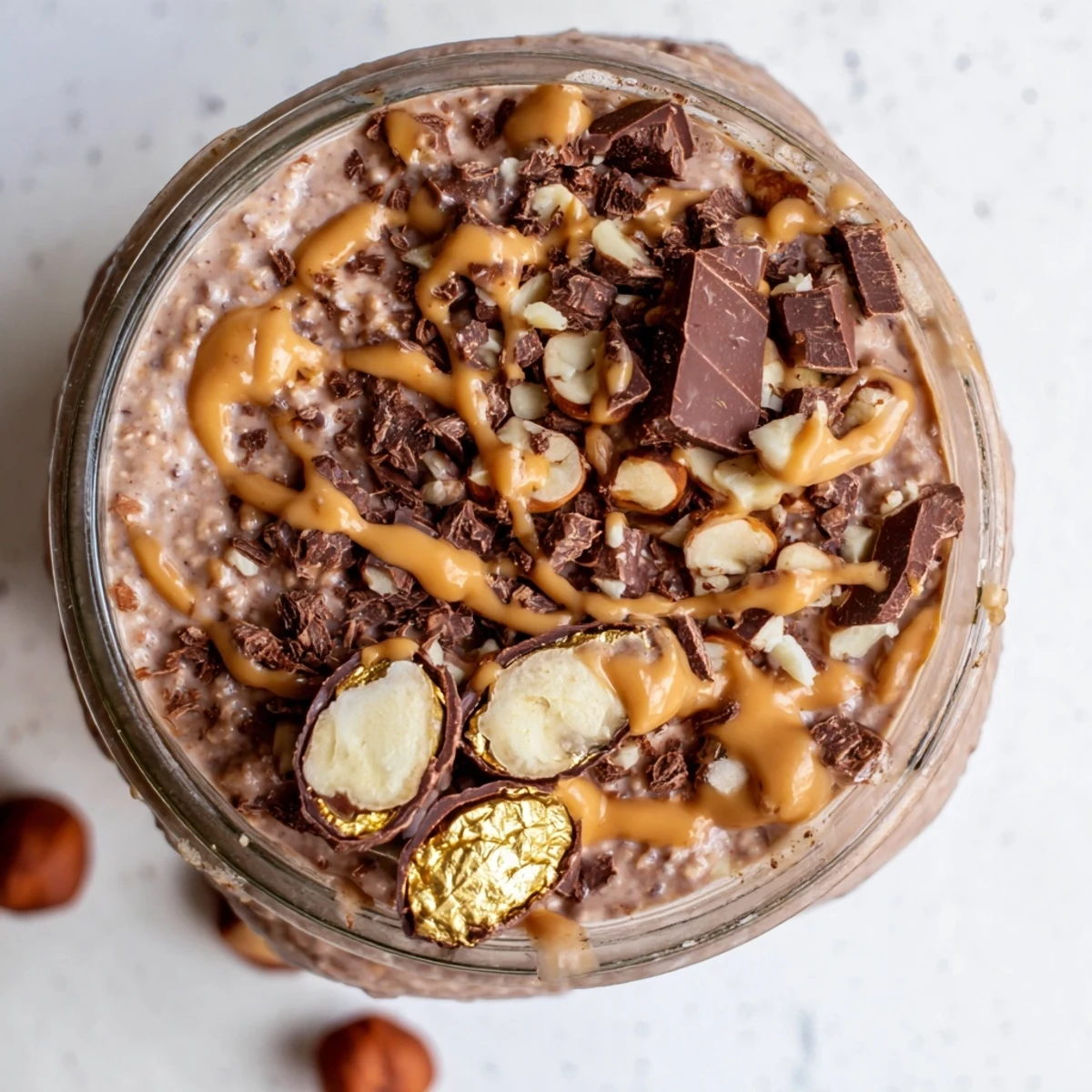 Healthy Ferrero Rocher Protein Overnight Oats topped with crunchy hazelnuts and chocolate shavings in a morning bowl.