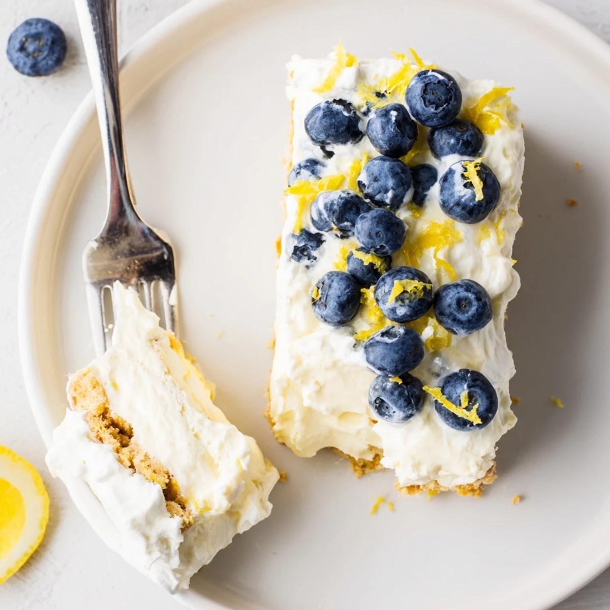 No bake lemon blueberry cream cake topped with fresh berries and lemon zest on a graham cracker crust