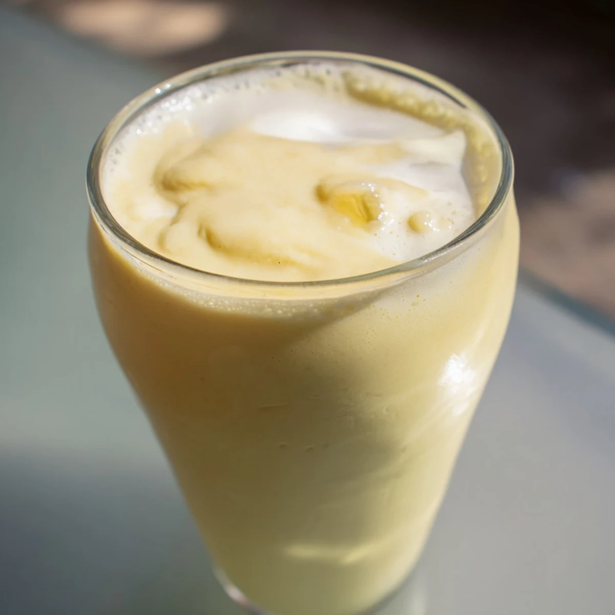 Golden durian smoothie recipe poured into tall glasses with fresh fruit garnish and condensation