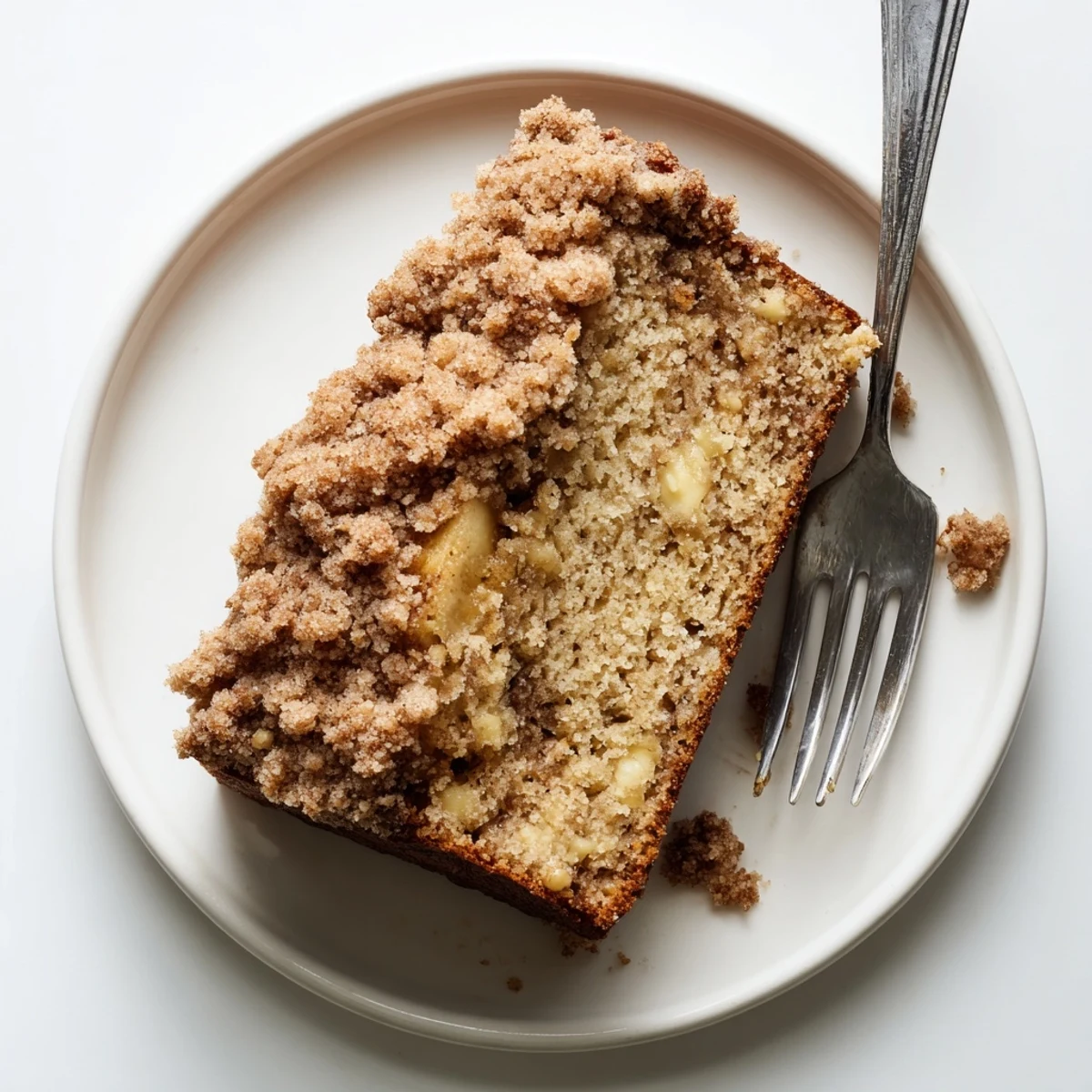 Moist banana bread slices sprinkled with buttery cinnamon crumbles on a white plate