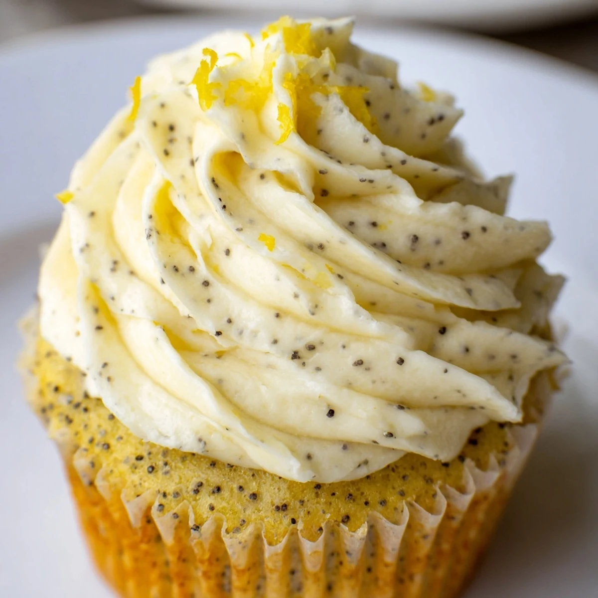 Freshly baked lemon poppy seed cupcakes sprinkled with zest on a white serving plate