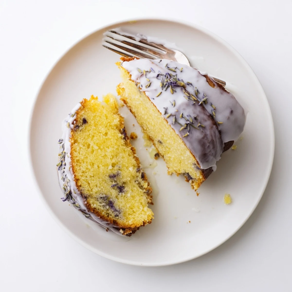 Moist lemon lavender cake drizzled with white glaze and sprinkled with dried purple lavender buds on a white plate