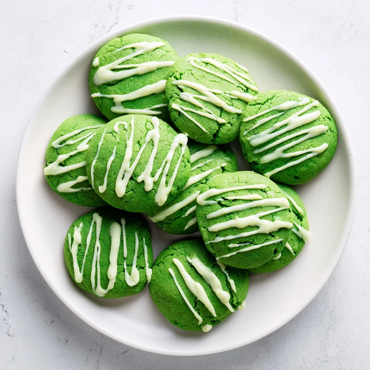 Soft green velvet cookies topped with melted white chocolate drizzle on a white plate