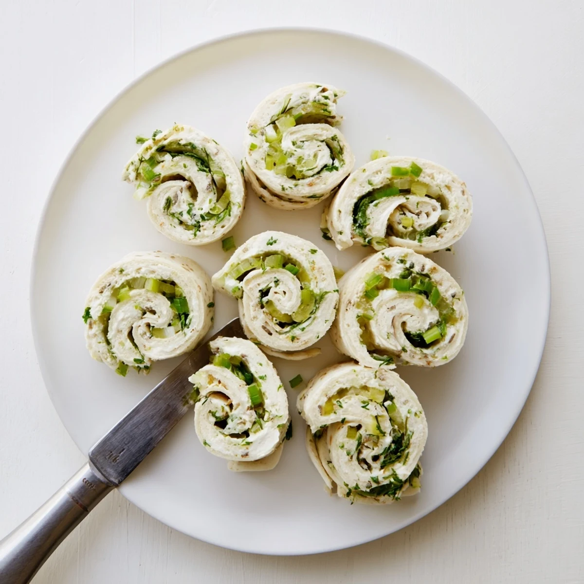 Tangy pickle dip pinwheels arranged on a serving platter showcasing vibrant green pickle pieces throughout the white cream cheese filling