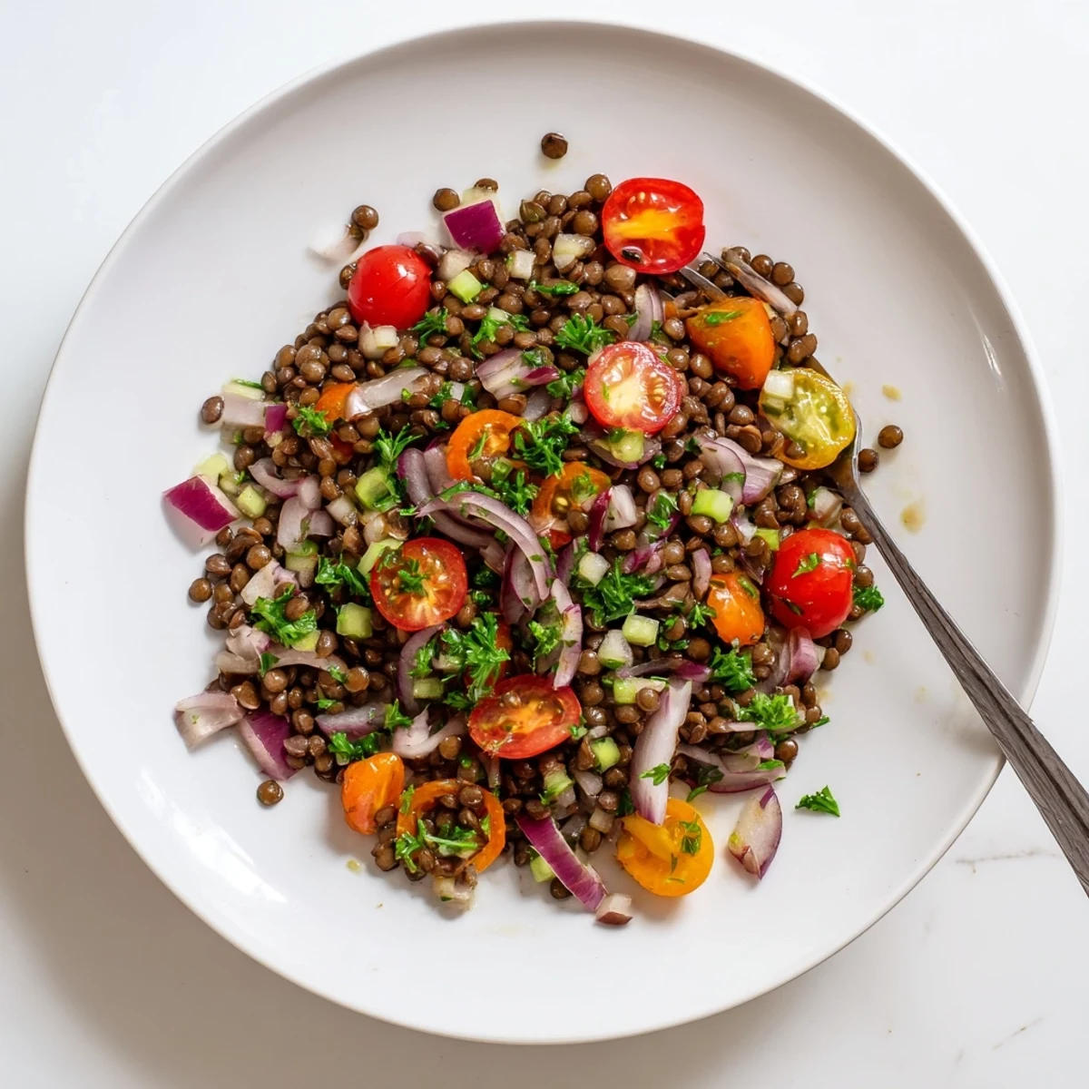 Colorful bowl of French lentil salad with cherry tomatoes and fresh herbs drizzled with tangy Dijon vinaigrette
