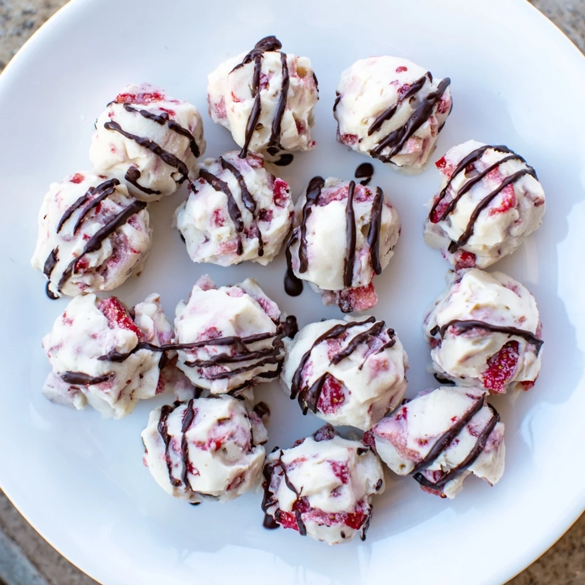 Frozen strawberry high protein yogurt bites topped with melted chocolate drizzle on a white plate for a healthy breakfast snack.