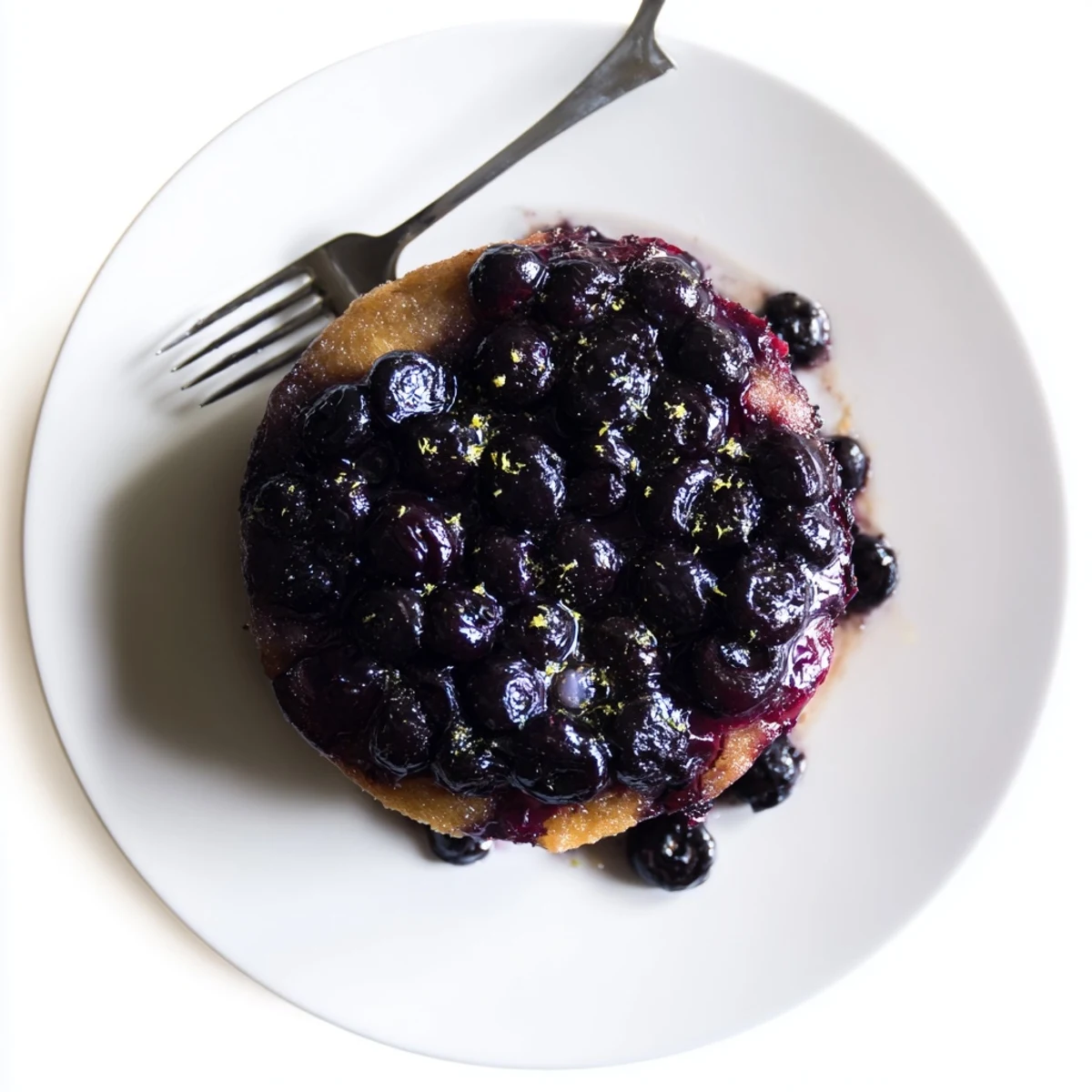 Golden blueberry upside down cake topped with glistening caramelized fresh blueberries on a white plate