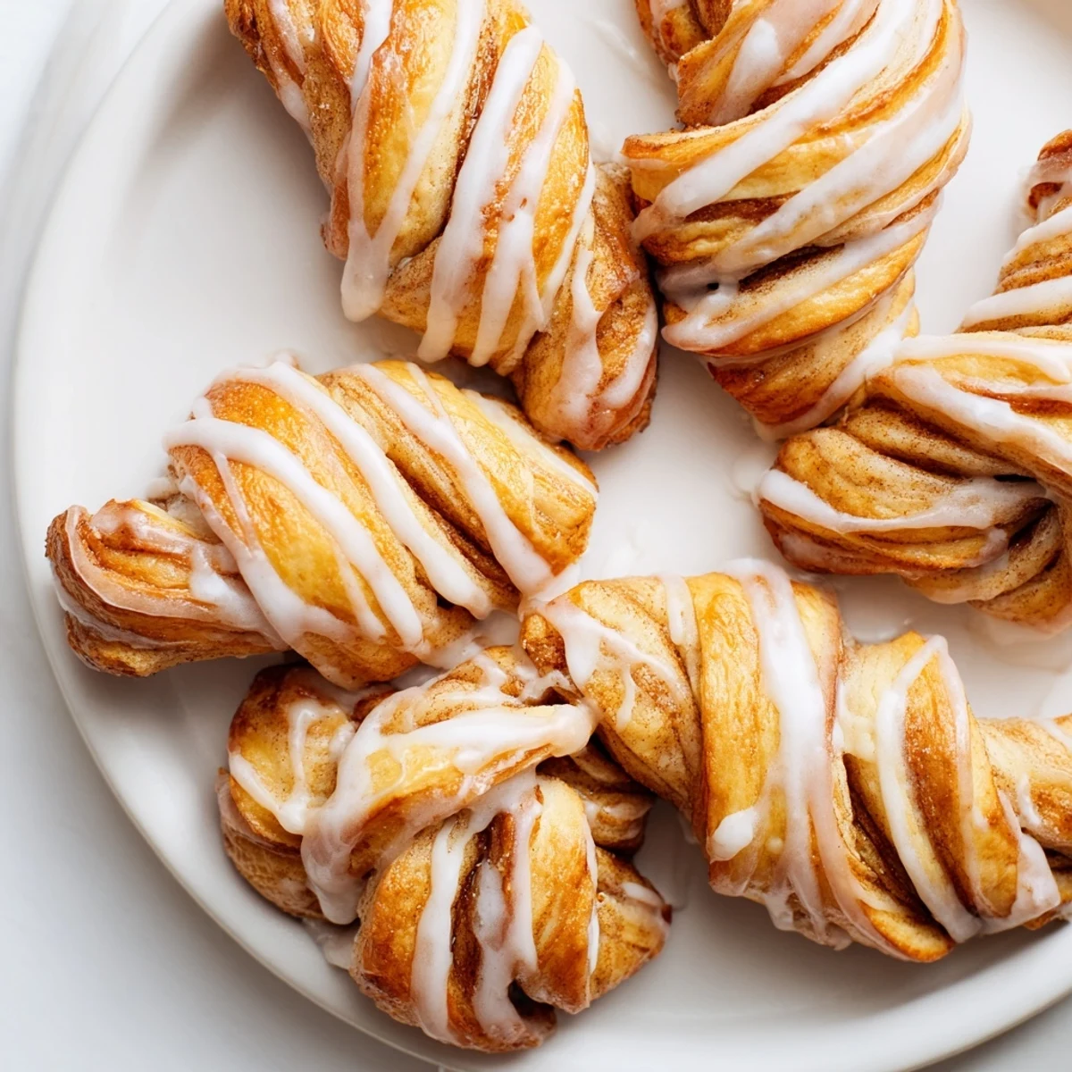 Golden sweet cinnamon twists drizzled with vanilla glaze on a white serving plate