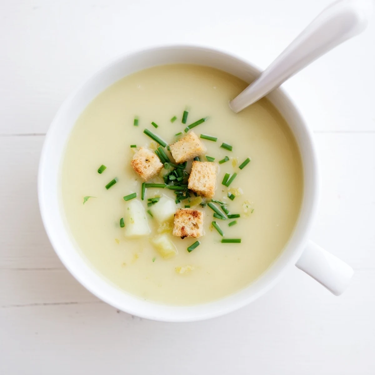 Creamy potato leek soup in a white bowl topped with fresh green chives and crispy croutons