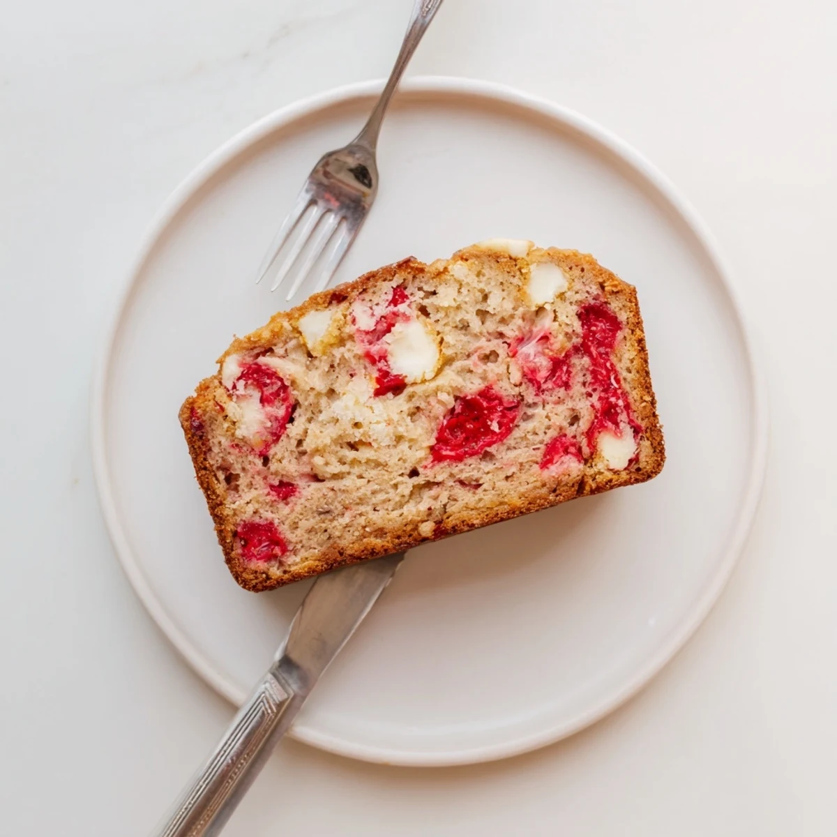 Thick slice of homemade sourdough strawberry white chocolate bread on a wooden board, showing flecks of tart strawberries and creamy white chips
