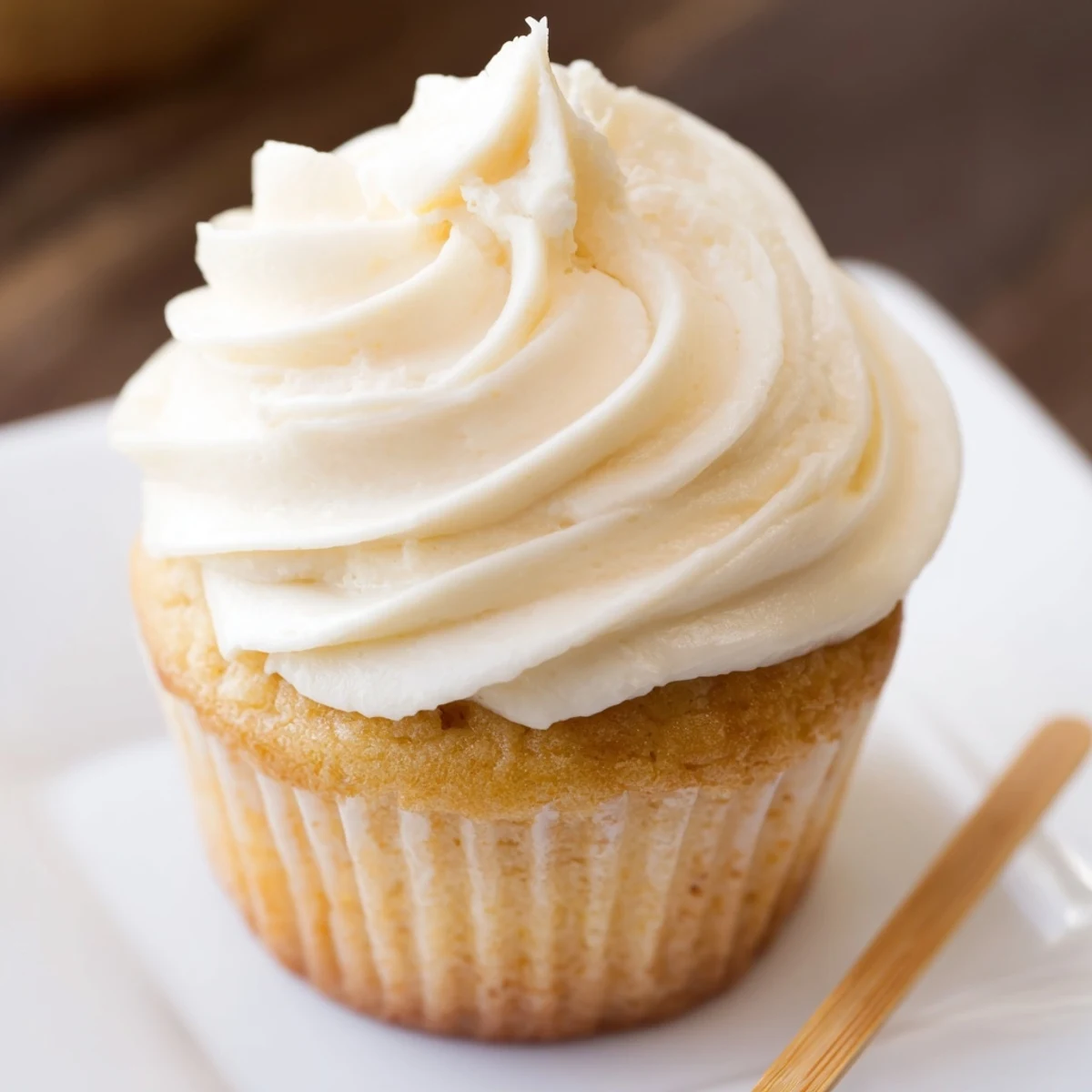Golden vanilla cupcakes topped with fluffy white buttercream frosting on a decorative serving plate