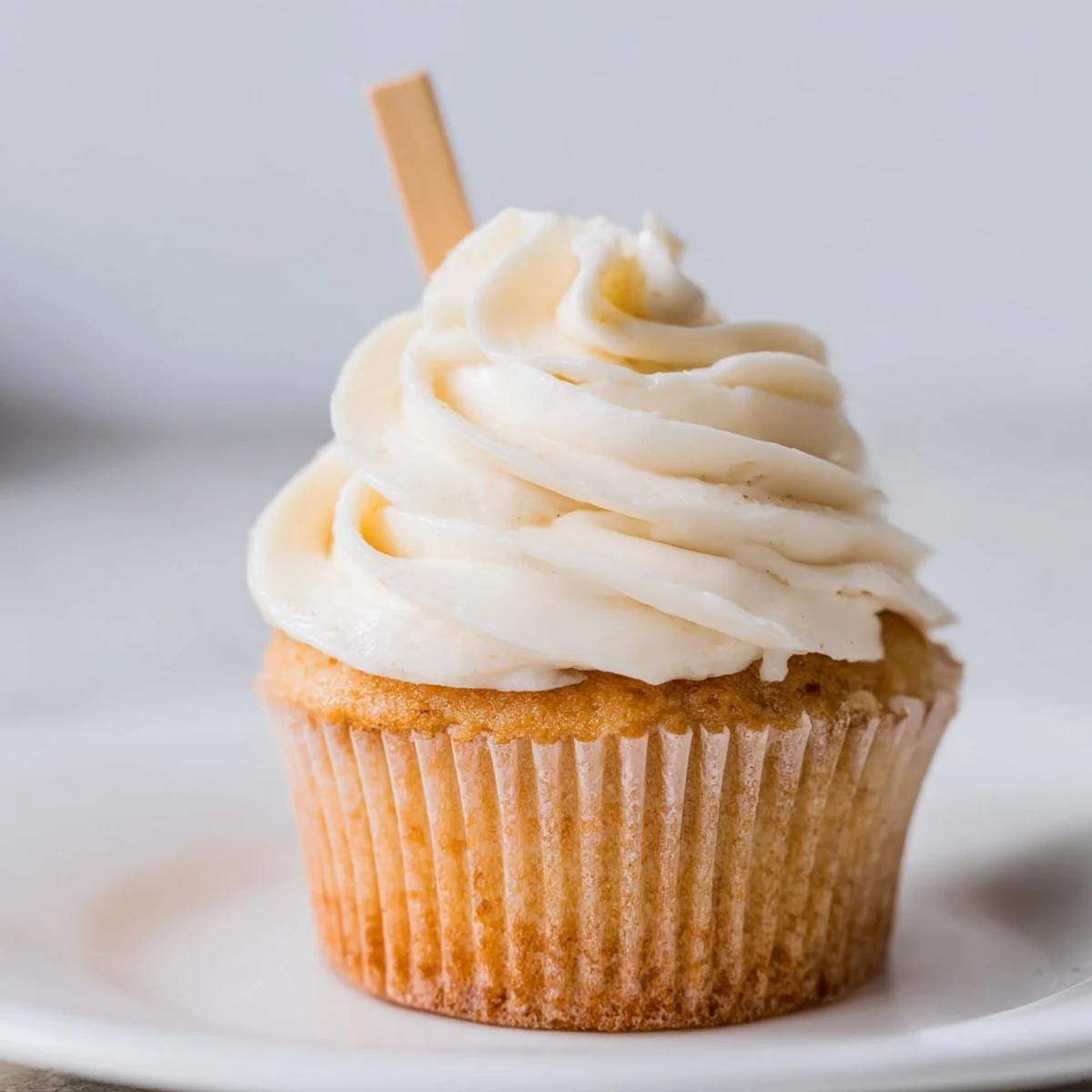 Batch of freshly baked vanilla cupcakes with smooth creamy frosting piped high atop each cake