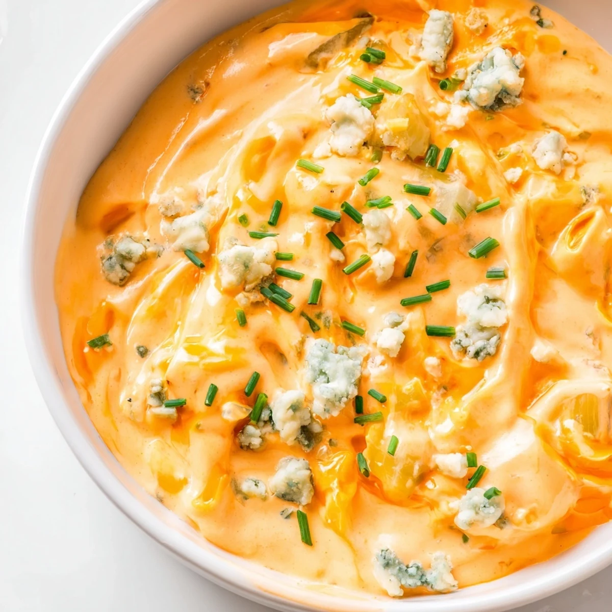 Tangy buffalo pickle dip topped with cheddar cheese and fresh chives on a rustic table