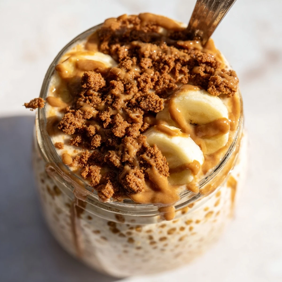 Creamy Biscoff overnight oats topped with crushed cookies and caramel drizzle in glass jar