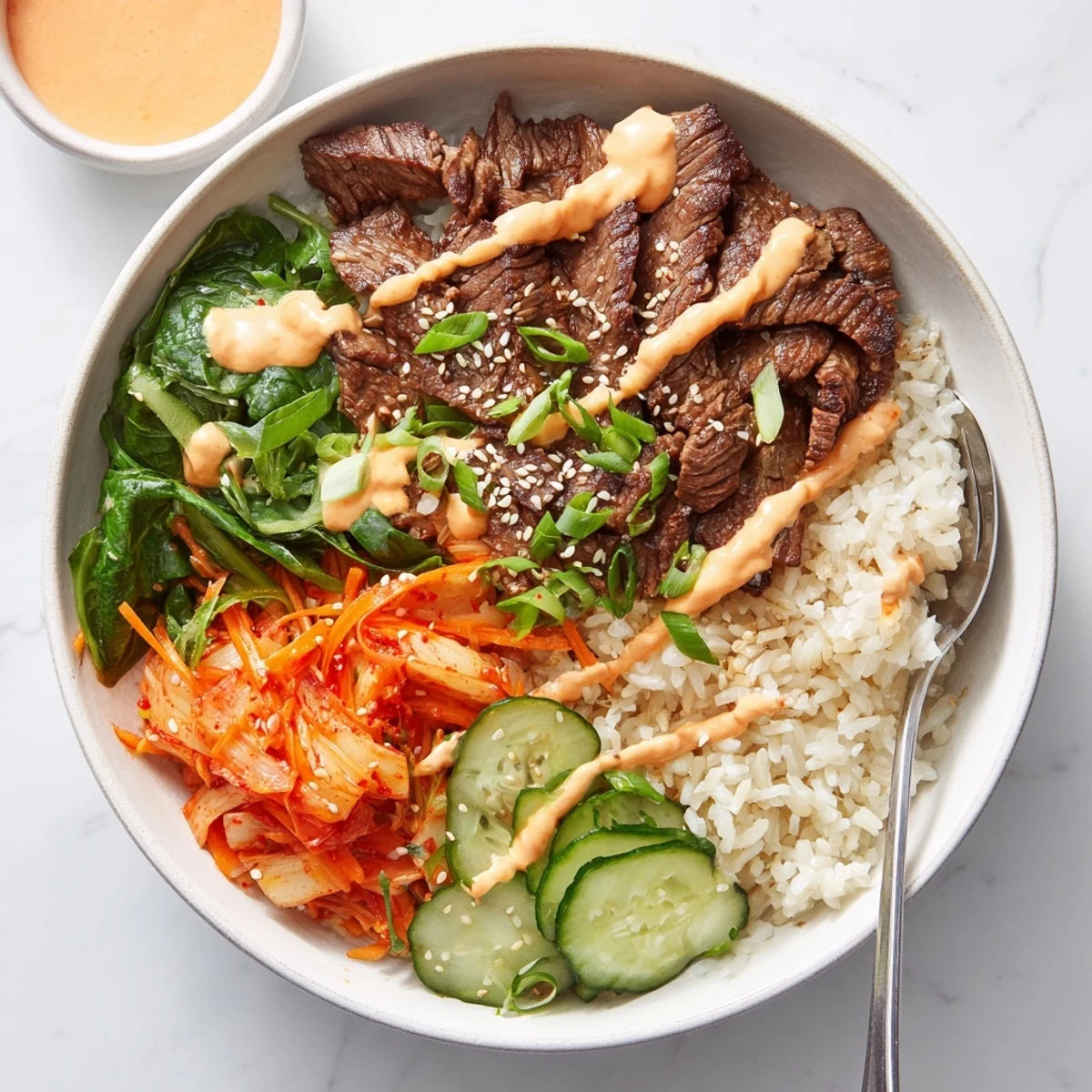 Sliced Korean BBQ steak in a loaded rice bowl topped with kimchi and spicy cream sauce