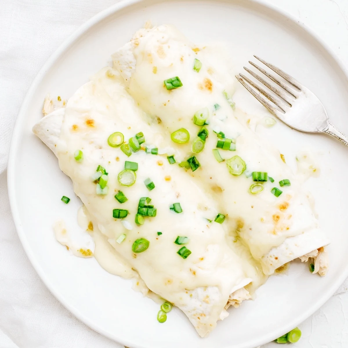 Sliced Creamy White Chicken Enchiladas on plate, garnished with cilantro and green onions