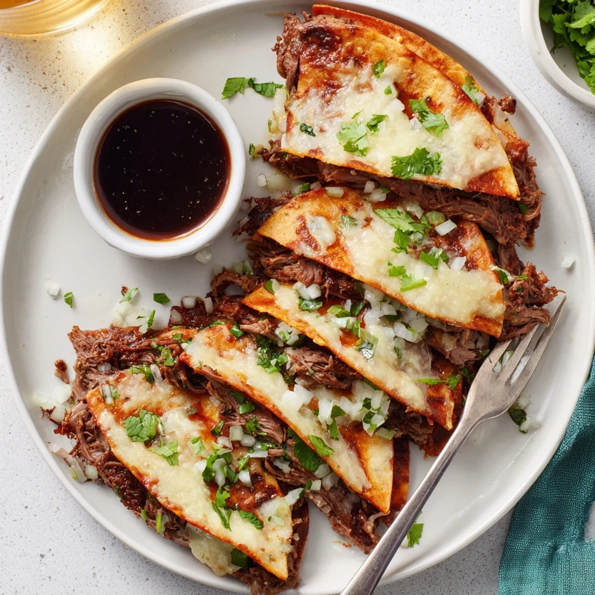 Birria Tacos served alongside rich consommé for dipping with fresh cilantro and lime garnish