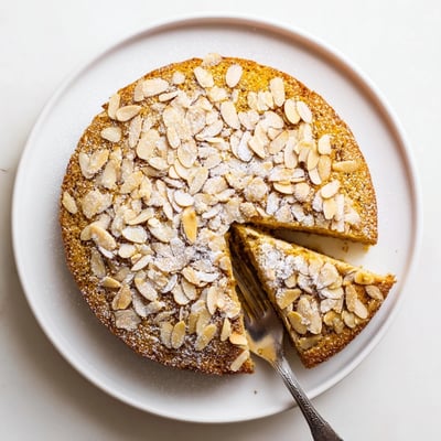 This moist Almond Cake shows golden edges and a tender crumb, cut to reveal the delicate almond interior on a plate.