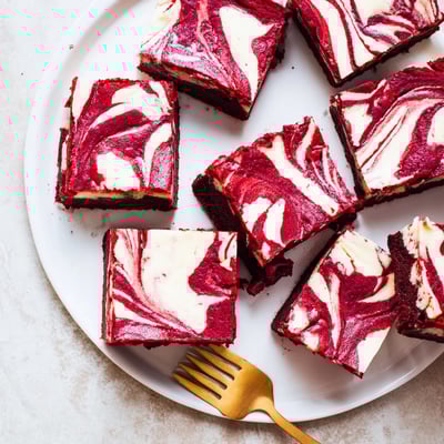Decadent Red Velvet Cheesecake Brownies swirled with creamy filling, cut into squares on a marble surface.