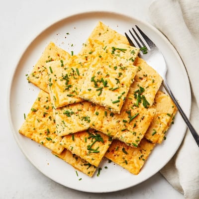 Crispy cheese and chive snack squares served warm on a rustic wooden board