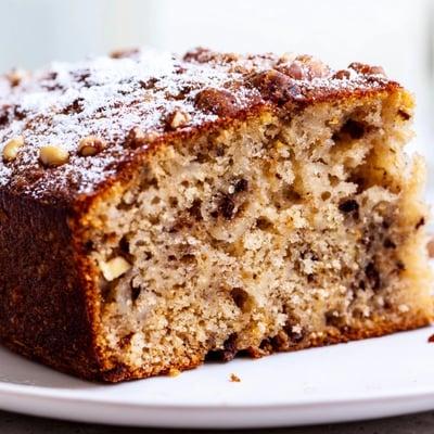 Moist banana cake sprinkled with powdered sugar beside a steaming cup of tea